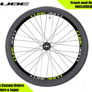 May include: A black mountain bike wheel with a yellow and black "CUBE BAND" decal on the rim. The text "Front and Rear INCLUDED" is in the upper right corner of the image. The text "We Do Custom Orders Colors & Logos" is in the lower left corner of the image.