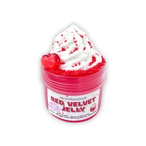 Pode incluir: Um recipiente de plástico vermelho cheio de slime de gelatina de veludo vermelho, coberto com slime branco e granulado vermelho. Um pingente em forma de coração vermelho fica na lateral. A etiqueta diz "Red Velvet Jelly" com o texto "Do Not Eat".