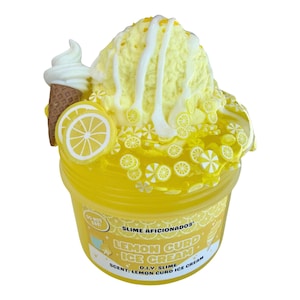 Può includere: Uno slime giallo in un contenitore di plastica trasparente con l'etichetta Slime Aficionados Lemon Curd Ice Cream. Lo slime è guarnito con una pallina gialla, glassa bianca, piccoli ciondoli a forma di limone e un mini cono marrone.