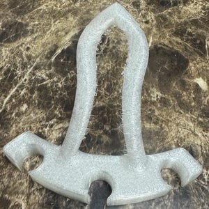 May include: A clear, 3D-printed object with a unique shape. It features a curved top and two flared, symmetrical sides with rounded cutouts. The object has a textured surface and is likely made of plastic.