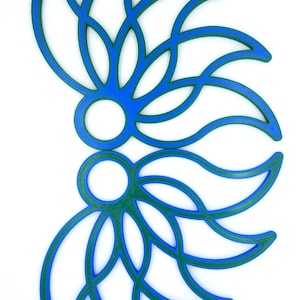 May include: Two abstract floral shapes in blue and green, each with a circular centre. The shapes are made up of overlapping curves and resemble a stylised flower.