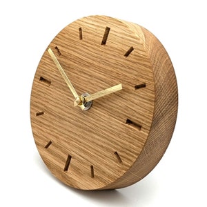 Könnte beinhalten: Eine runde Holzuhr mit goldenen Zeigern und römischen Ziffern. Die Uhr ist aus hellbraunem Eichenholz gefertigt und hat eine natürliche Holzoptik.