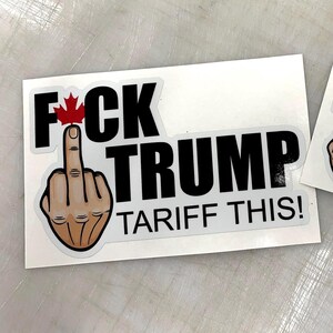 May include: A white sticker with black text that reads "FCK TRUMP TARIFF THIS!" with a middle finger emoji and a Canadian flag above the "F".