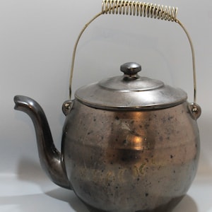 May include: A vintage metal teapot with a spring handle and a dark gray finish. The teapot has a round body and a lid with a knob on top.
