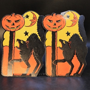 May include: Two identical vintage cardboard Halloween decorations featuring a black cat arching its back, a bright orange jack-o'-lantern on a post, a yellow crescent moon with a face, and black stars against a yellow and orange background.