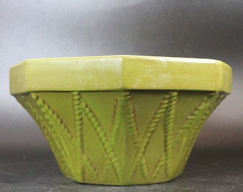 May include: A green octagonal ceramic planter with a textured design of woven strands. The planter has a wide opening and a slightly flared base.