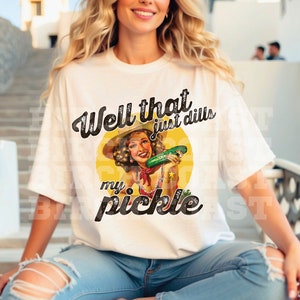 Pu&ograve; includere: Maglietta bianca con una grafica in stile vintage di una donna che tiene un cetriolo. Il testo sulla maglietta recita "Well that just dills my pickle."