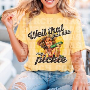 Pu&ograve; includere: Maglietta gialla con un'illustrazione vintage di una donna che tiene un cetriolo. Il testo "Well that just dills my pickle" &egrave; stampato sulla maglietta.