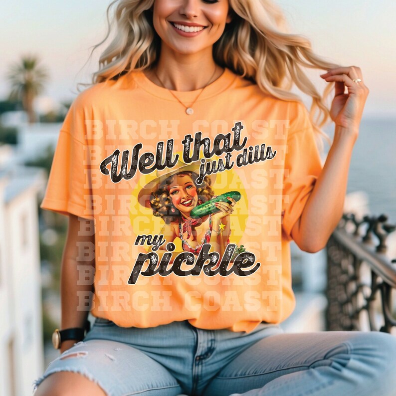 Pu&ograve; includere: Una donna indossa una maglietta arancione con una grafica vintage di una donna che tiene un cetriolo. Il testo sulla maglietta recita "Well that just dills my pickle".
