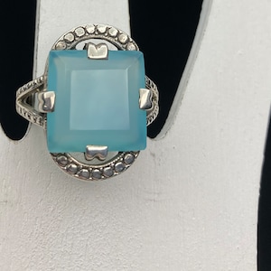 May include: A silver ring with a light blue square gemstone set in a decorative silver frame.