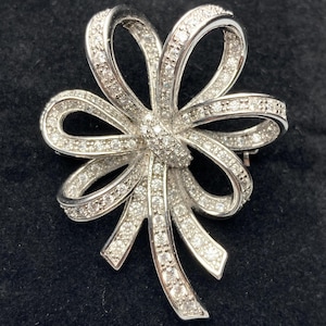 May include: A silver bow brooch with clear rhinestones. The bow is made of multiple loops and has a long, flowing tail.