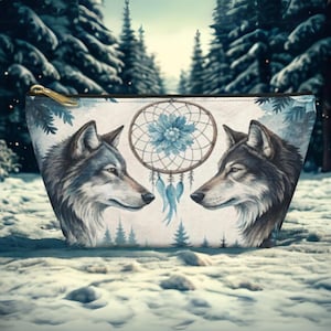 May include: A white zippered pouch with a dreamcatcher design and two grey wolves facing each other. The dreamcatcher has blue and brown feathers and a blue flower in the center. The background is a snowy forest.