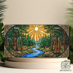 May include: License plate featuring a stained-glass design of a forest scene with deer, a river, and a bright sun. The artwork is framed with a decorative border. The color palette includes greens, blues, browns, and yellows.