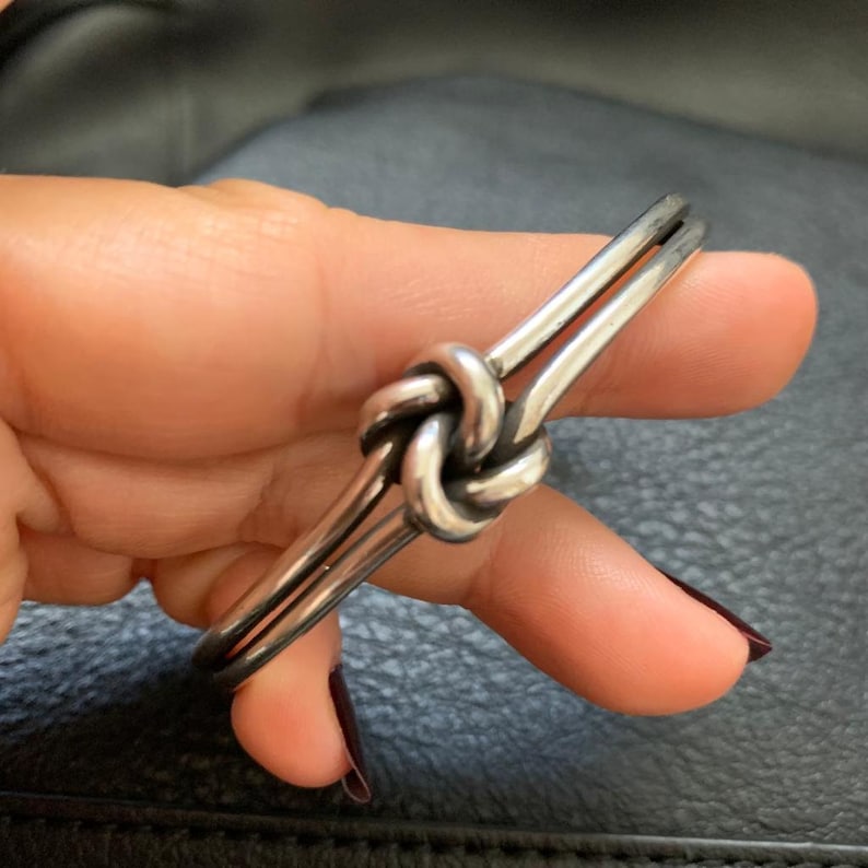 May include: A silver knot bracelet with a double band design. The knot is a simple, elegant design.