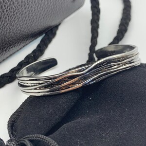 May include: A silver bracelet with a wavy, braided design. The bracelet is on a black velvet pouch.