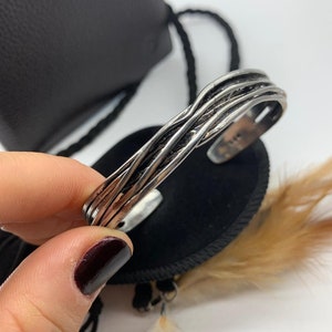 May include: A silver bracelet with a braided design. The bracelet is open and has a slightly curved shape.