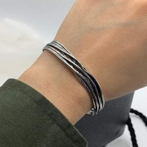 May include: A silver bracelet with a woven design. The bracelet is made of multiple strands of metal that are twisted together.