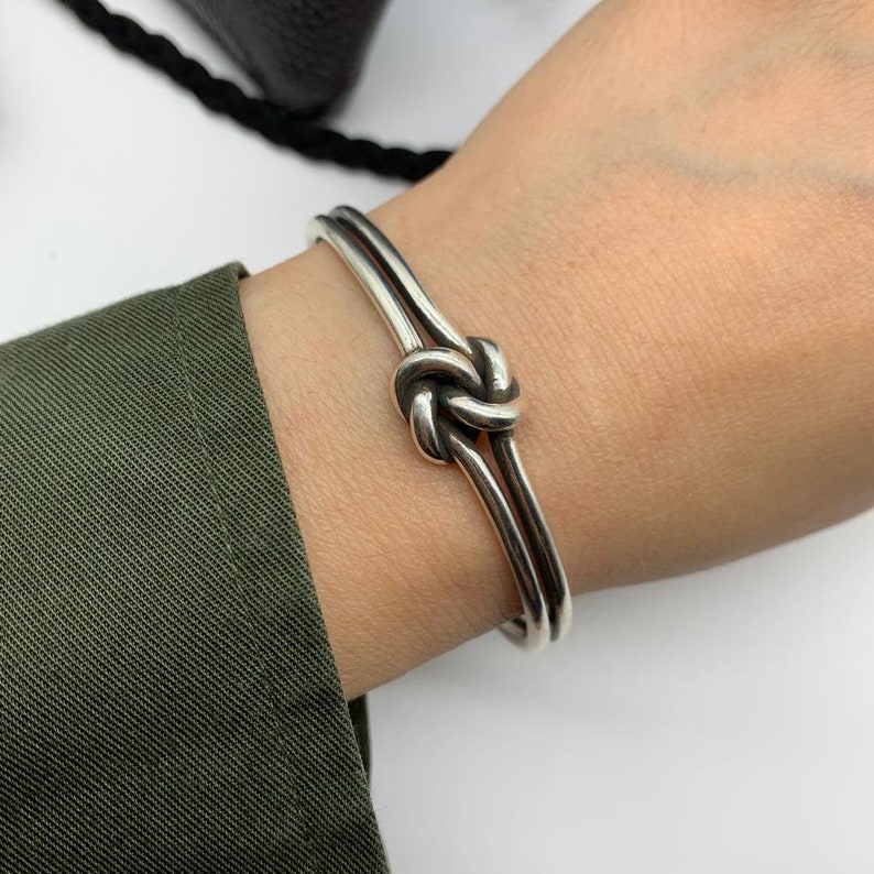 May include: A silver knot bracelet with a double band design. The knot is a simple, elegant design.