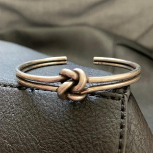 May include: A silver knot bracelet with a double band design. The knot is a simple, elegant design.