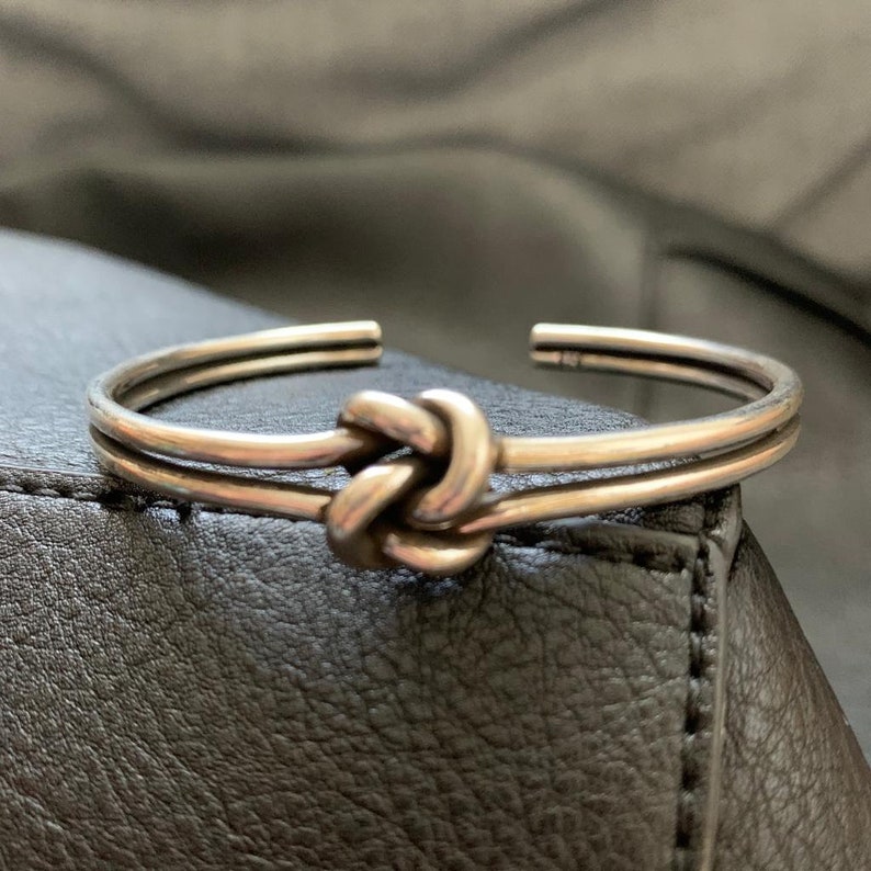 May include: A silver knot bracelet with a double band design. The knot is a simple, elegant design.