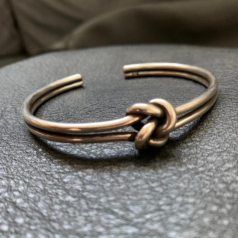 May include: A silver knot bracelet with a double band design. The knot is a simple, elegant design.