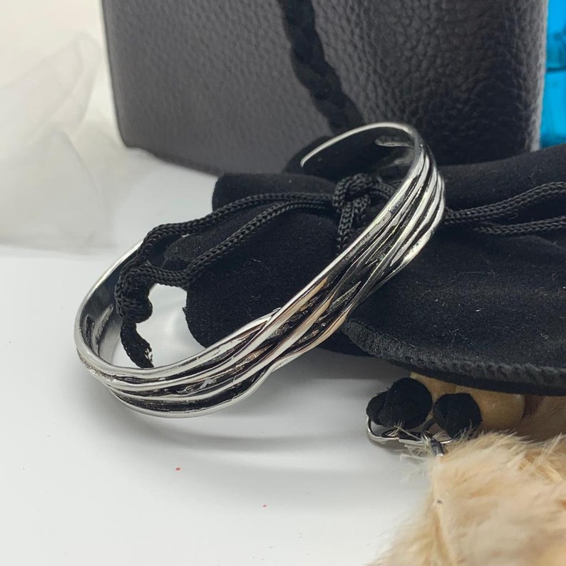 May include: A silver bangle bracelet with a woven design. The bracelet is on a black velvet pouch.