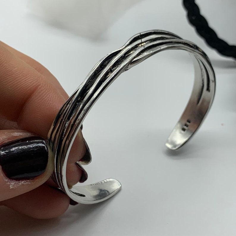 May include: Silver bracelet with a braided design. The bracelet is open and has a slightly curved shape.