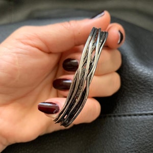 May include: A silver bracelet with a braided design. The bracelet is made of multiple strands of silver wire that are woven together to create a unique and intricate pattern.
