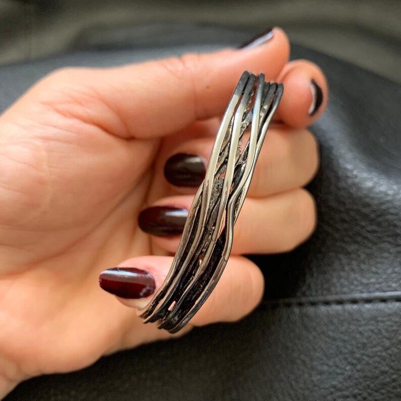 May include: A silver bracelet with a braided design. The bracelet is made of multiple strands of silver wire that are woven together to create a unique and intricate pattern.