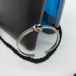 May include: A silver bracelet with a knotted design. The bracelet is made of two bands of metal that are twisted together to form a knot.