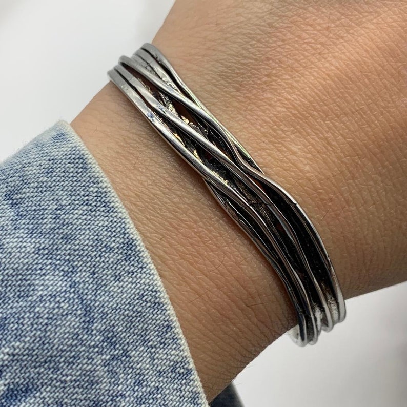 May include: A silver bracelet with a woven design. The bracelet is made of multiple strands of silver that are twisted together.