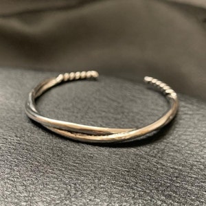 Peut inclure: Un bracelet jonc torsadé en argent. Le bracelet est composé de deux brins de métal torsadés ensemble.