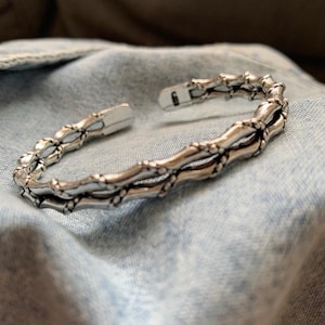 May include: Silver bracelet with a woven design. The bracelet is open and has a hinged clasp.