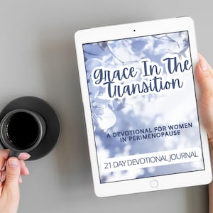 May include: A digital tablet displays the title "Grace In The Transition" with the subtitle "A Devotional for Women in Perimenopause." A cup of coffee sits on a saucer to the left. The tablet is held in a person's hand.