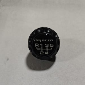 May include: Black gear shift knob with a silver 'synchro' logo and gear pattern. The gear pattern shows 'R135' and '24' in a diamond shape.