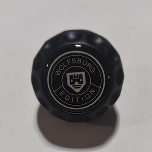 May include: Black round knob with a silver emblem that reads "Wolfsburg Edition" and a stylized castle graphic.