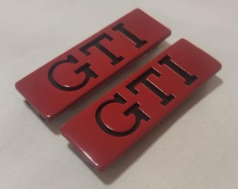 May include: Two red rectangular car emblems with the word "GTI" in black lettering.