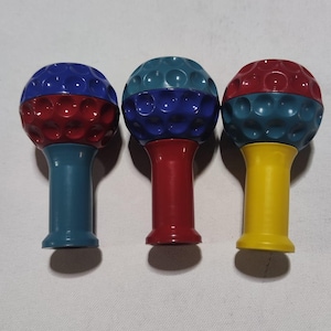 Pu&ograve; includere: Tre strumenti da massaggio a forma di palla da golf con superfici testurizzate. Gli strumenti sono rosso, blu e giallo.