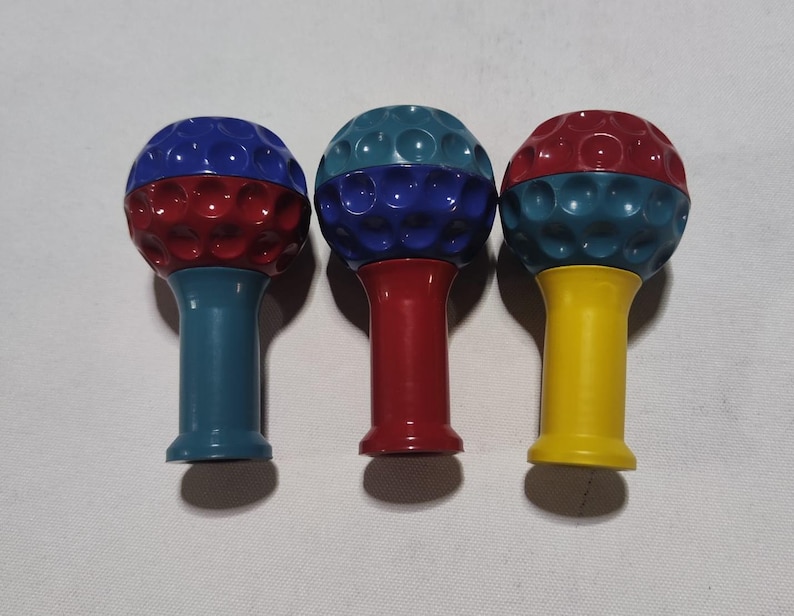 Pu&ograve; includere: Tre strumenti da massaggio a forma di palla da golf con superfici testurizzate. Gli strumenti sono rosso, blu e giallo.