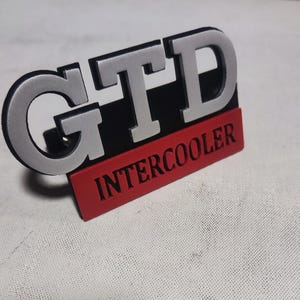 May include: Silver GTD emblem with a black background and a red "INTERCOOLER" label.