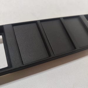 May include: A black plastic panel with five rectangular slots. The slots are evenly spaced and have a slightly raised edge.