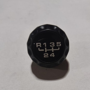 Op de afbeelding: Zwarte versnellingspookknop met witte letters die het versnellingschema aangeven: R, 1, 3, 5, 2, 4.