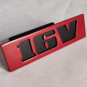 May include: Red and black car emblem with the text "16V" in black.