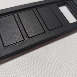 Peut inclure: Panneau en plastique noir avec quatre ouvertures rectangulaires et une plus petite ouverture rectangulaire. Le panneau a une surface texturée.