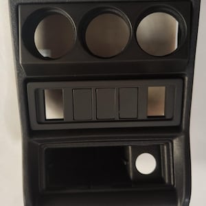 May include: Black plastic dashboard panel with three round openings and five rectangular slots.