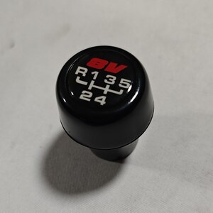 May include: Black gear shift knob with a red 8V logo and white numbers and letters indicating gear positions: R, 1, 3, 5, 2, 4.