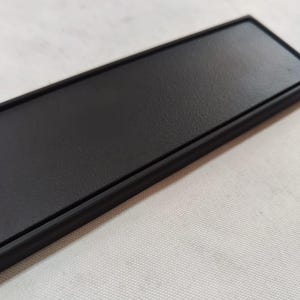 Peut inclure: Une plaque rectangulaire noire avec une surface lisse et texturée et une bordure noire.