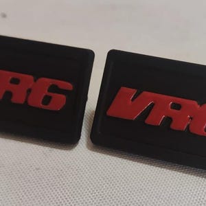 Pode incluir: Dois remendos retangulares pretos com o texto "VR6" em letras vermelhas.