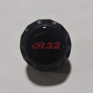 Peut inclure: Bouton en plastique noir avec un logo "R32" rouge.