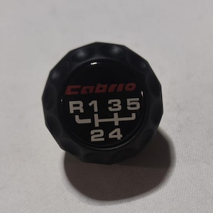 May include: Black gear shift knob with a red "Cabrio" logo and white numbers "R135 24" printed on it.